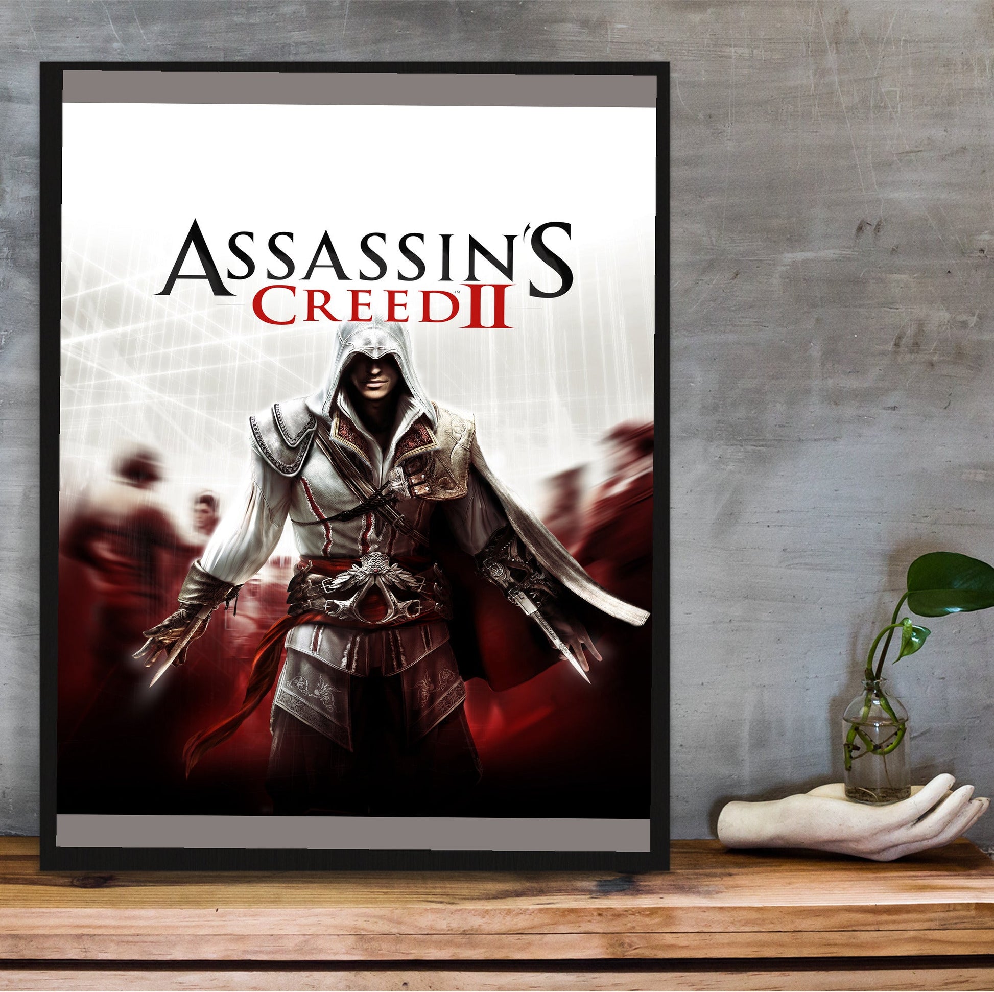 Assassin's Creed II key art in a black frame on a wooden shelf against concrete