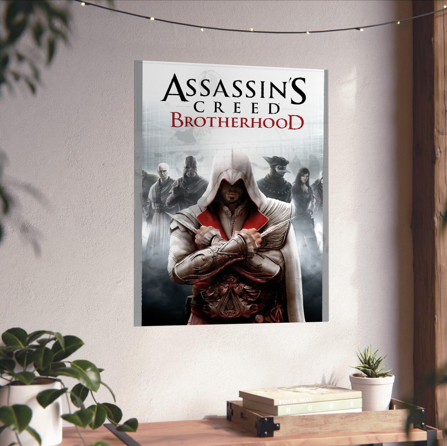 Assassin's Creed Brotherhood cover art unframed on a white wall above a desk