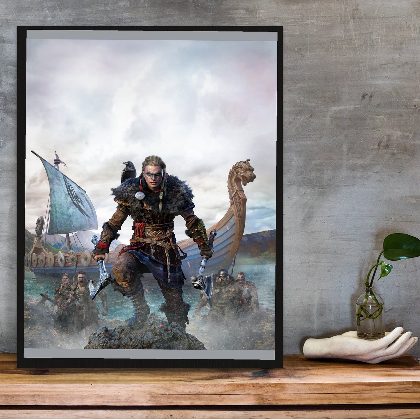 Assassin's Creed Valhalla female Eivor cover art in a black frame on a wooden shelf against concrete