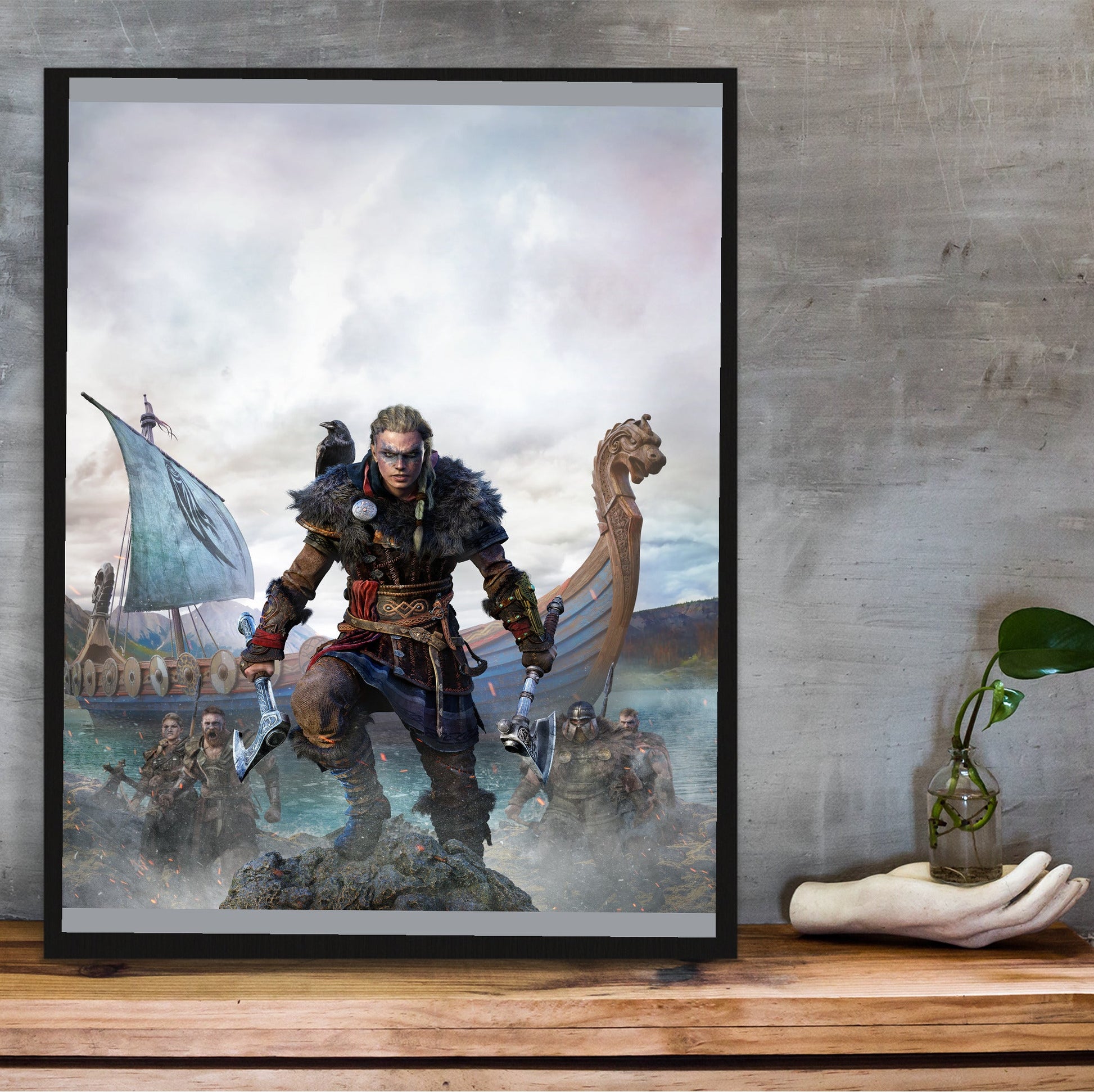 Assassin's Creed Valhalla female Eivor cover art in a black frame on a wooden shelf against concrete