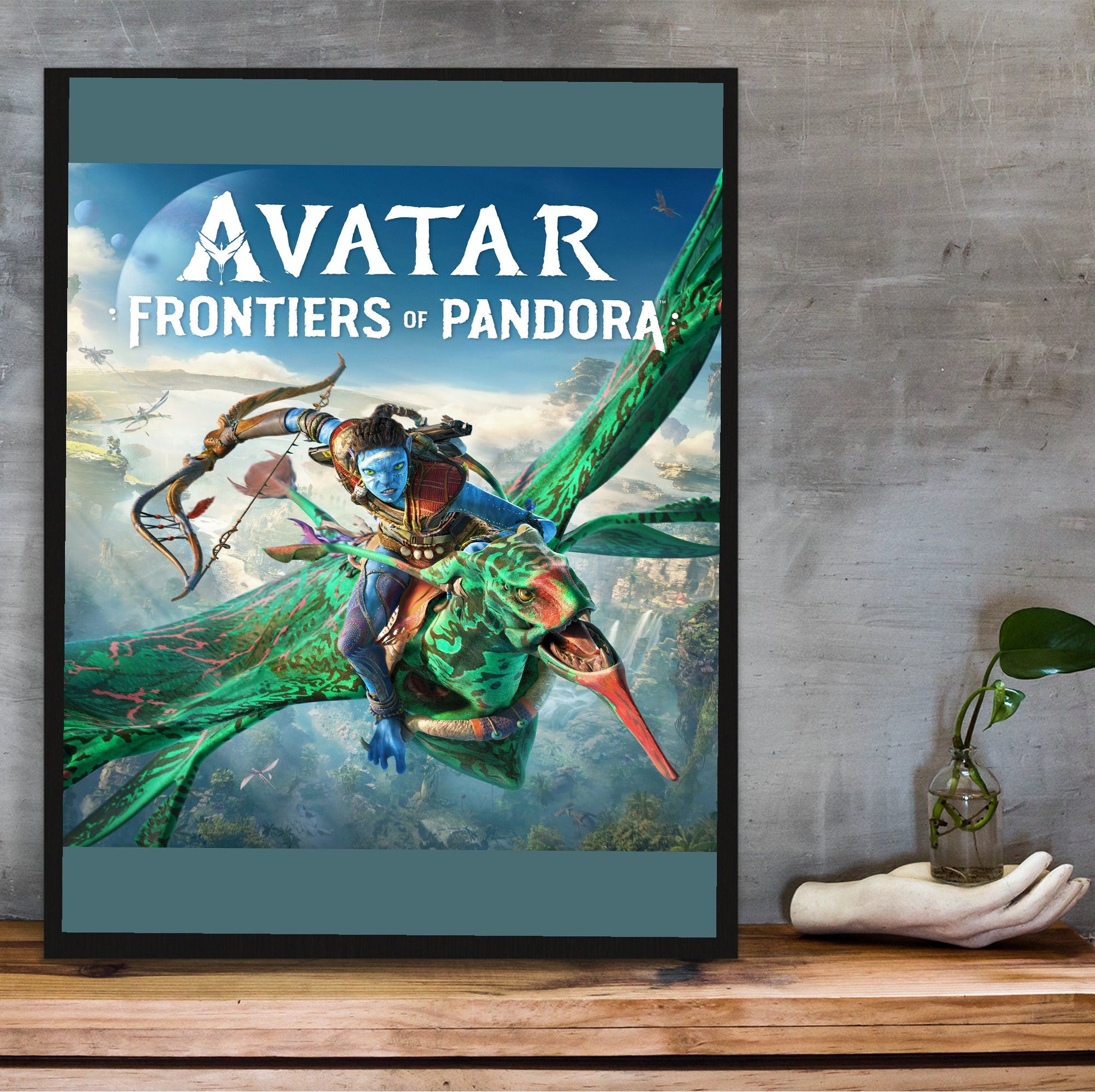 Avatar Frontiers of Pandora Official Cover Art in a black frame on a wooden shelf against concrete