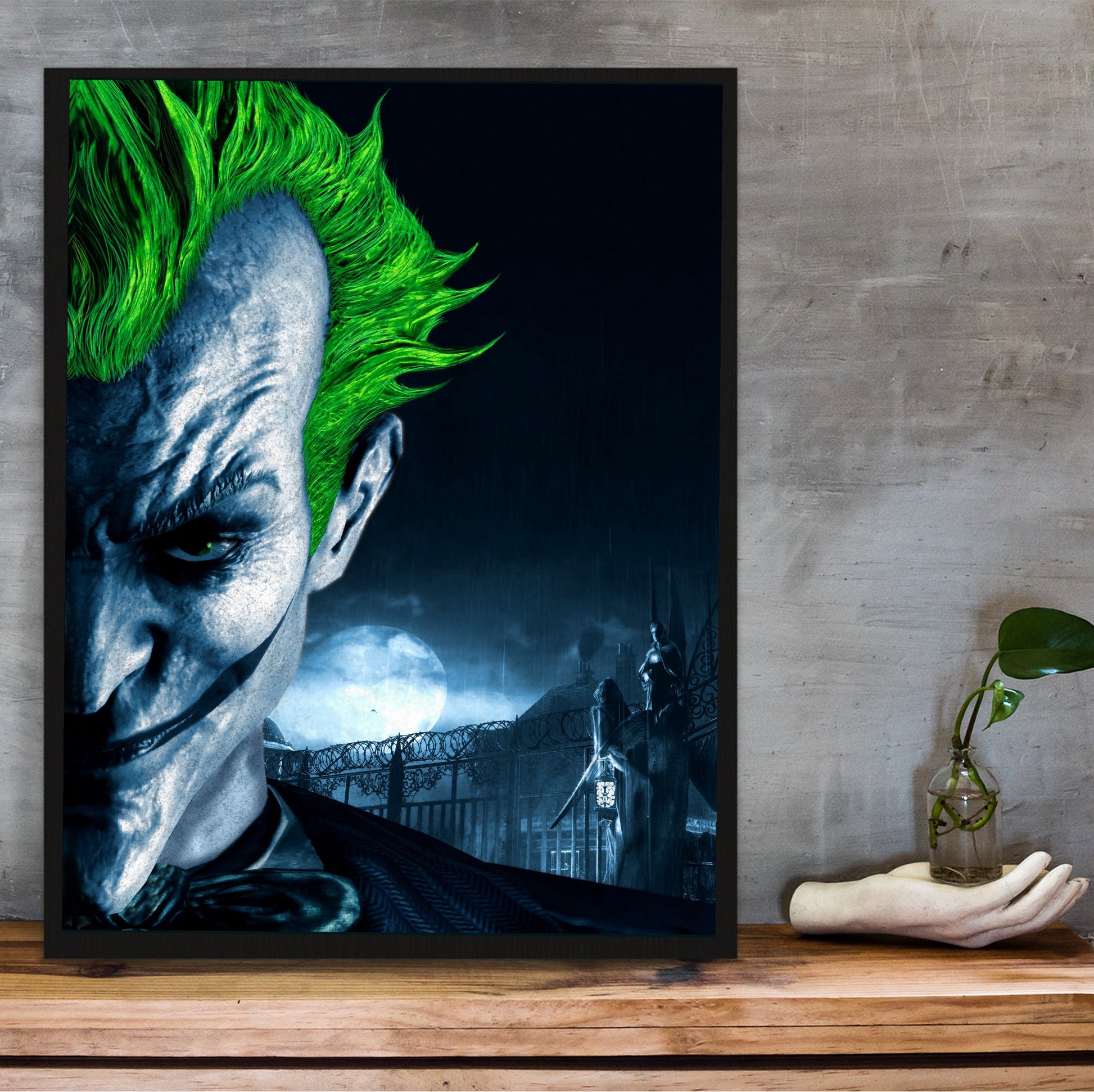 Batman Arkham Asylum Joker promo art poster in a black frame on a wooden shelf against concrete