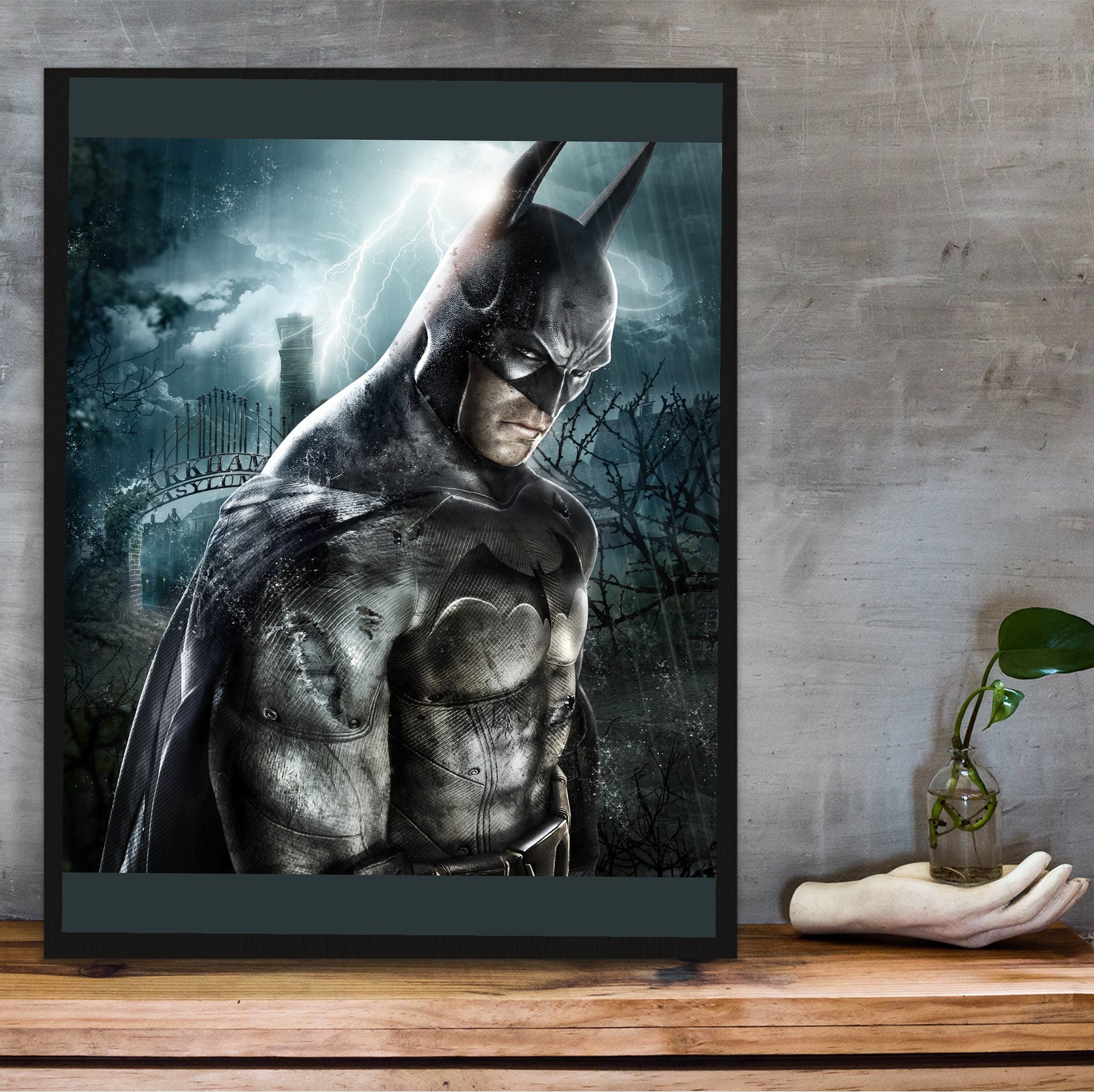Batman Arkham Asylum official key art poster in a black frame on a wooden shelf against concrete