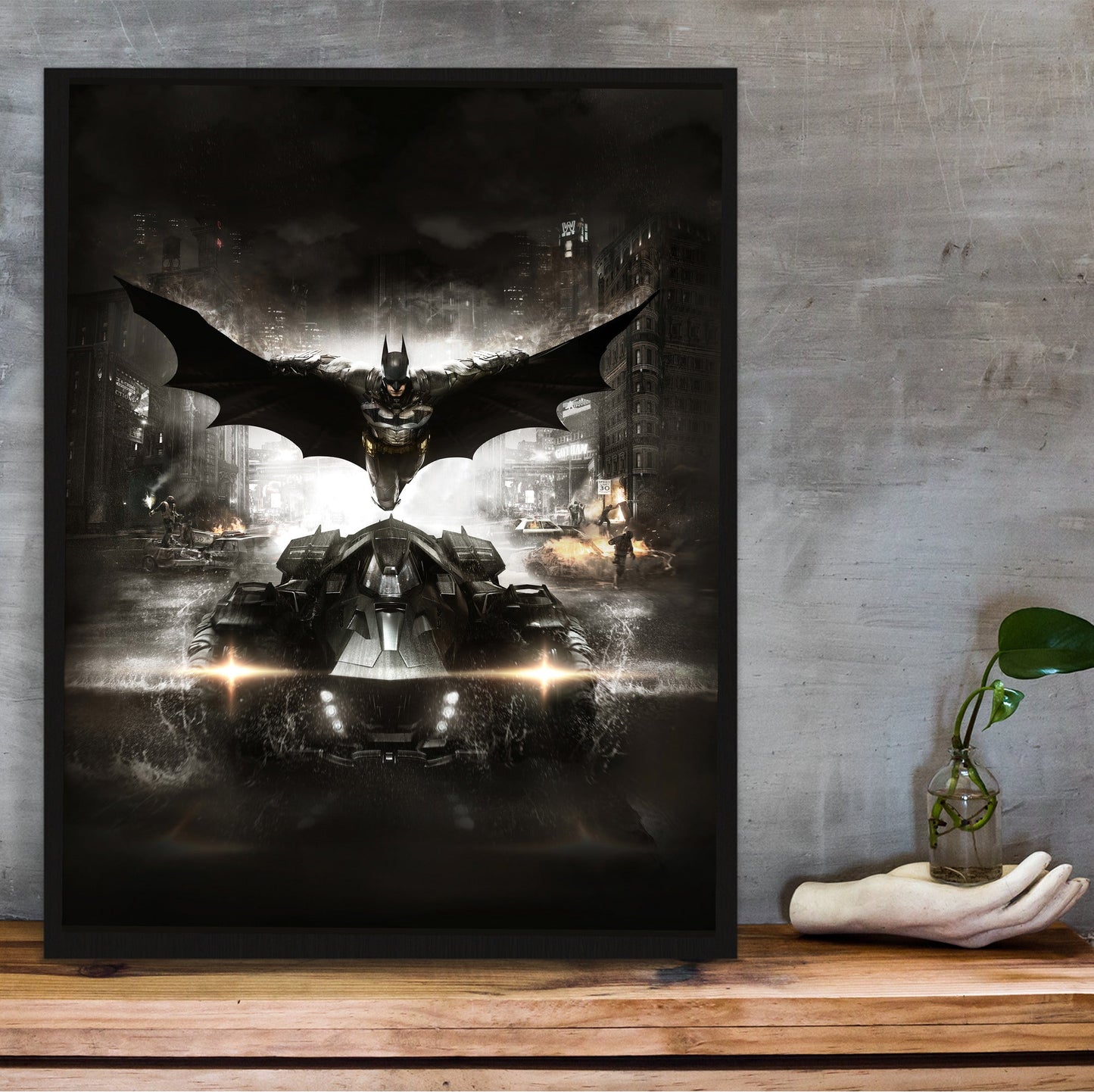 Batman Arkham Knight Batman and Batmobile key art poster in a black frame on a wooden shelf against concrete