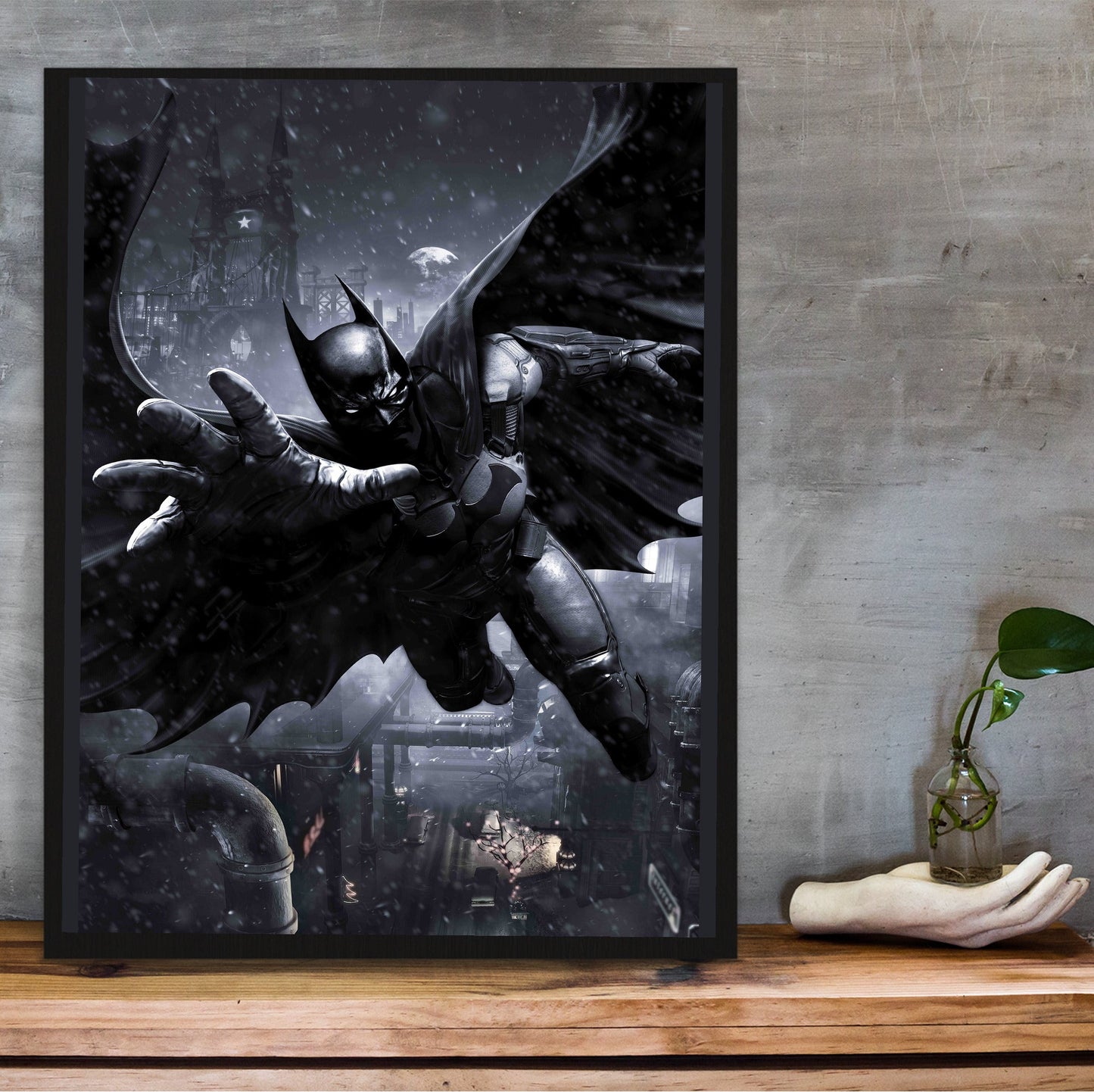Batman Arkham Origins Batman gliding promo art poster in a black frame on a wooden shelf against concrete