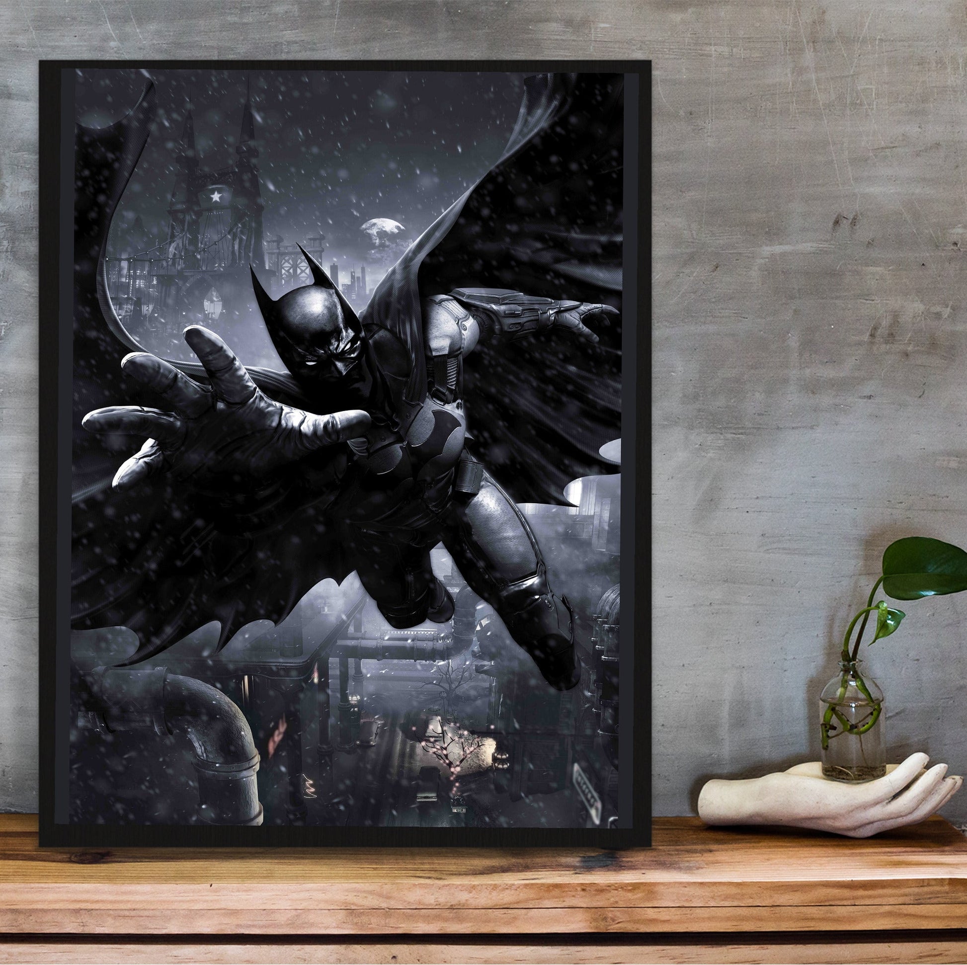 Batman Arkham Origins Batman gliding promo art poster in a black frame on a wooden shelf against concrete