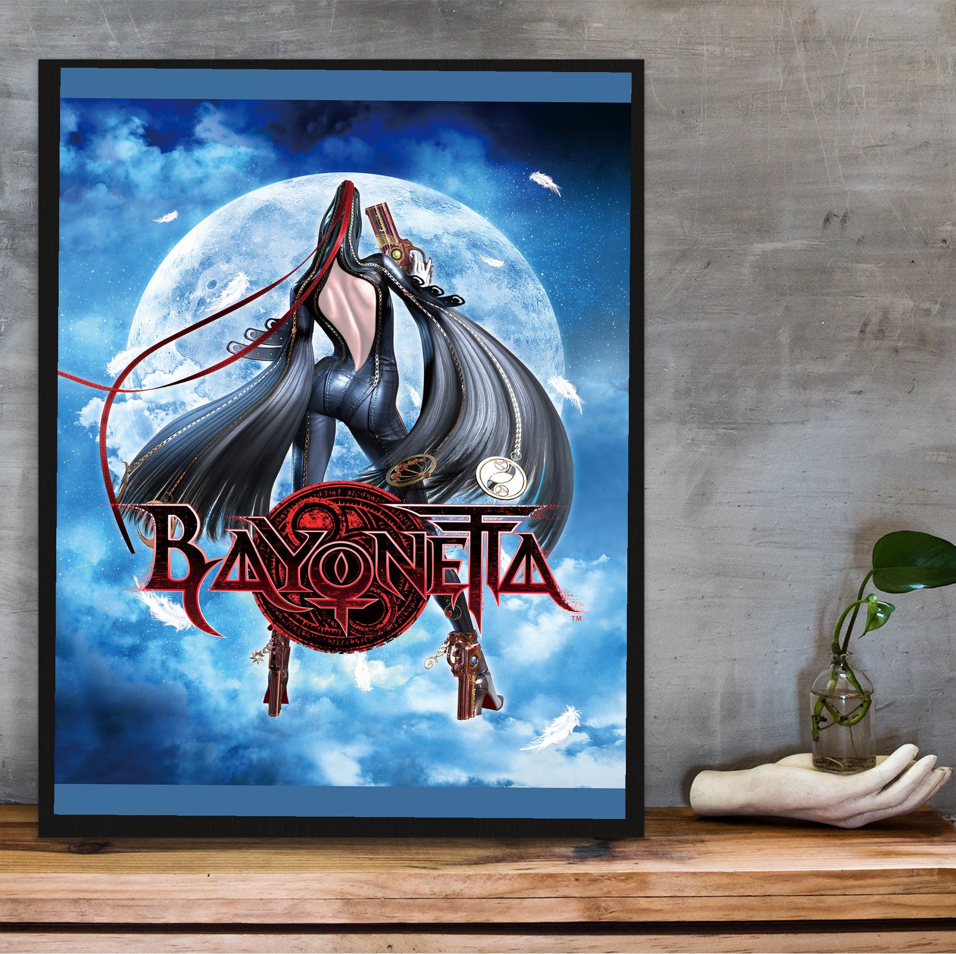 Bayonetta moonlight key art with logo poster in a black frame on a wooden shelf against concrete