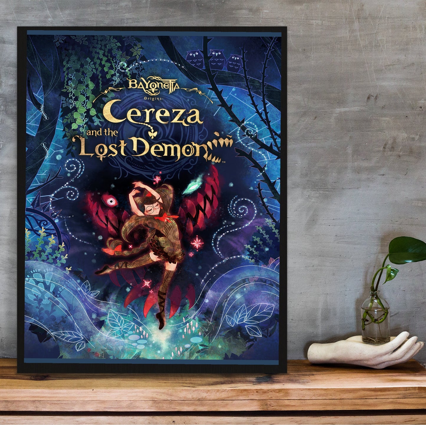 Bayonetta Origins Cereza and the Lost Demon cover art poster in a black frame on a wooden shelf against concrete