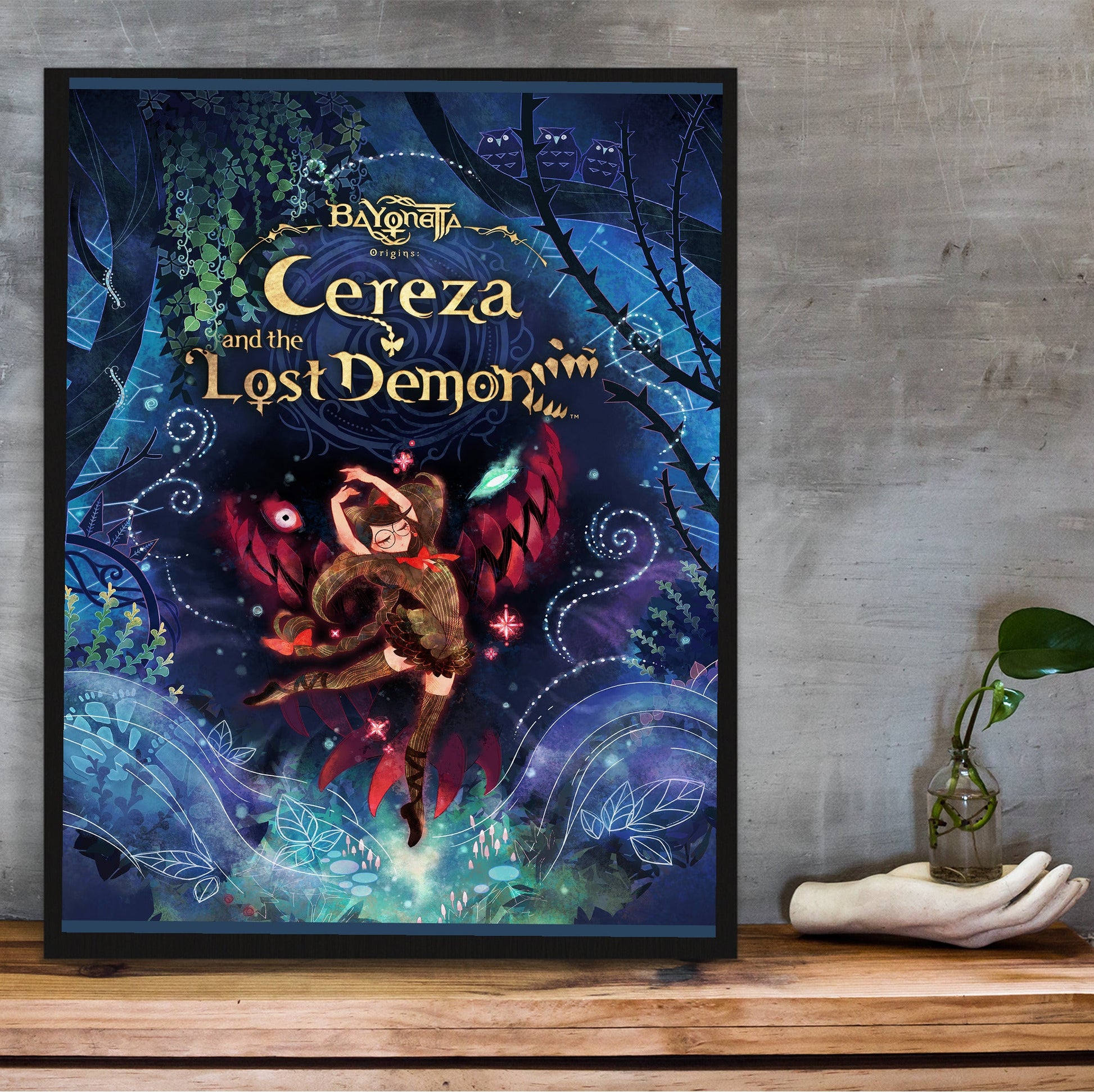Bayonetta Origins Cereza and the Lost Demon cover art poster in a black frame on a wooden shelf against concrete