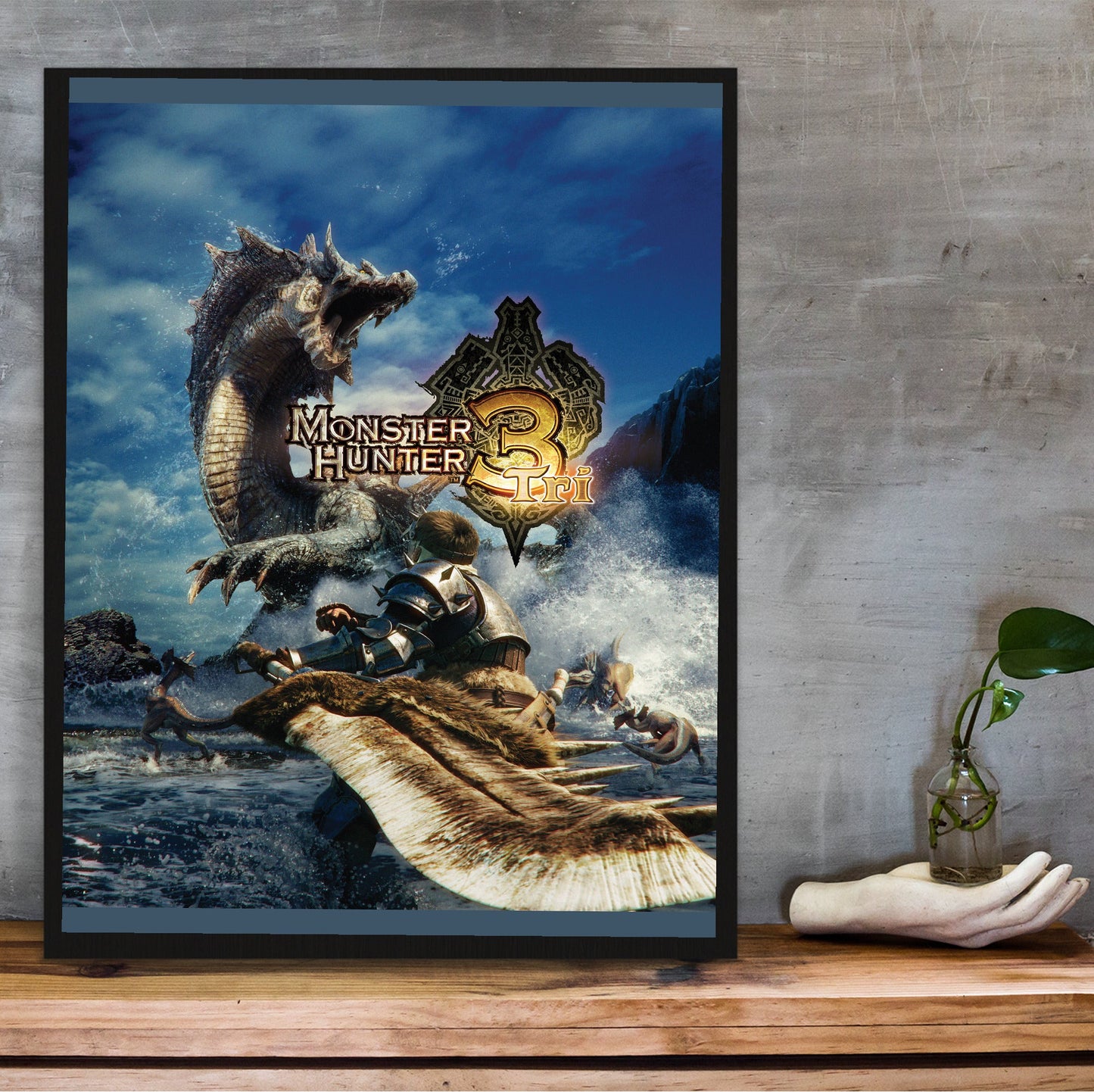 Monster Hunter Tri cover art with logo in a black frame on a wooden shelf against concrete