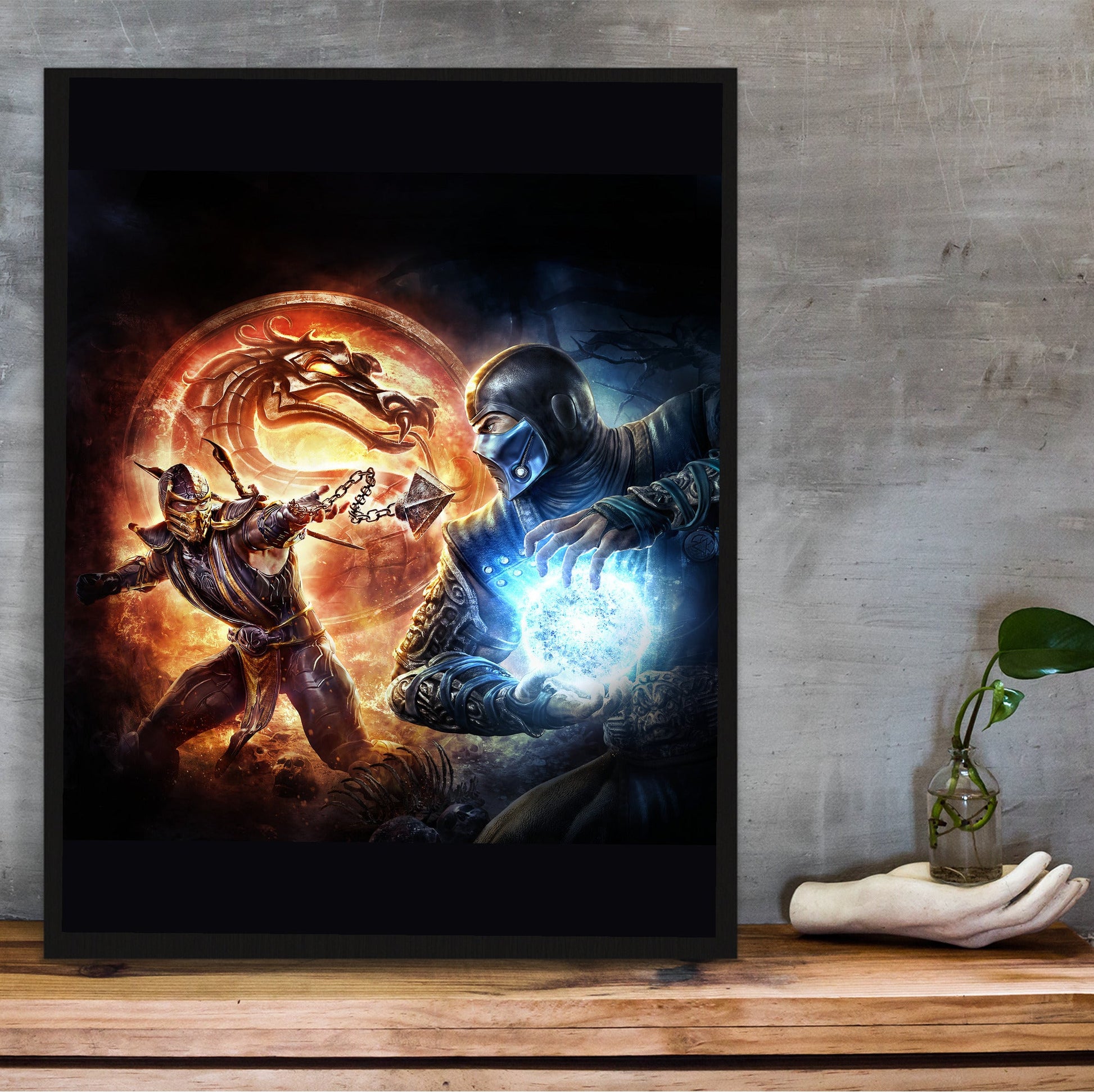 Mortal Kombat 9 Scorpion vs Sub-Zero cover art in a black frame on a wooden shelf against concrete