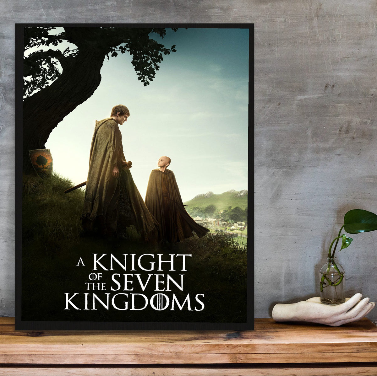 A Knight of the Seven Kingdoms Key Art poster in a black frame on a wooden shelf against concrete