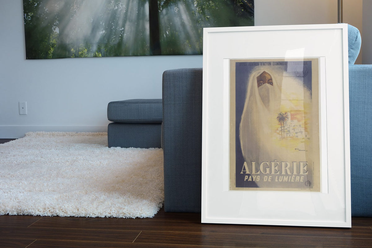 Algerie Pays de Lumiere poster leaning beside a blue sofa