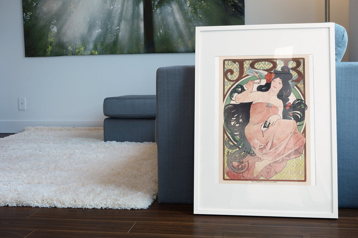 Alphonse Mucha JOB 1898 rolling papers poster in a white frame leaning beside a blue sofa