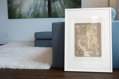 Alphonse Mucha JOB cigarette paper poster in a white frame leaning beside a blue sofa