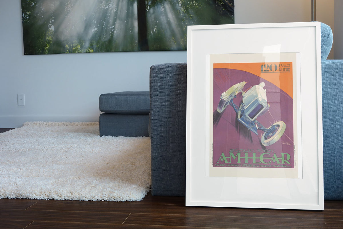 Amilcar Grand Sport poster in a white frame leaning beside a blue sofa
