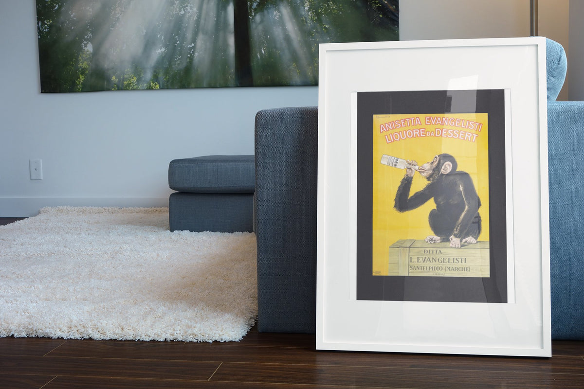 Anisetta Evangelisti 1925 monkey poster in a white frame leaning beside a blue sofa