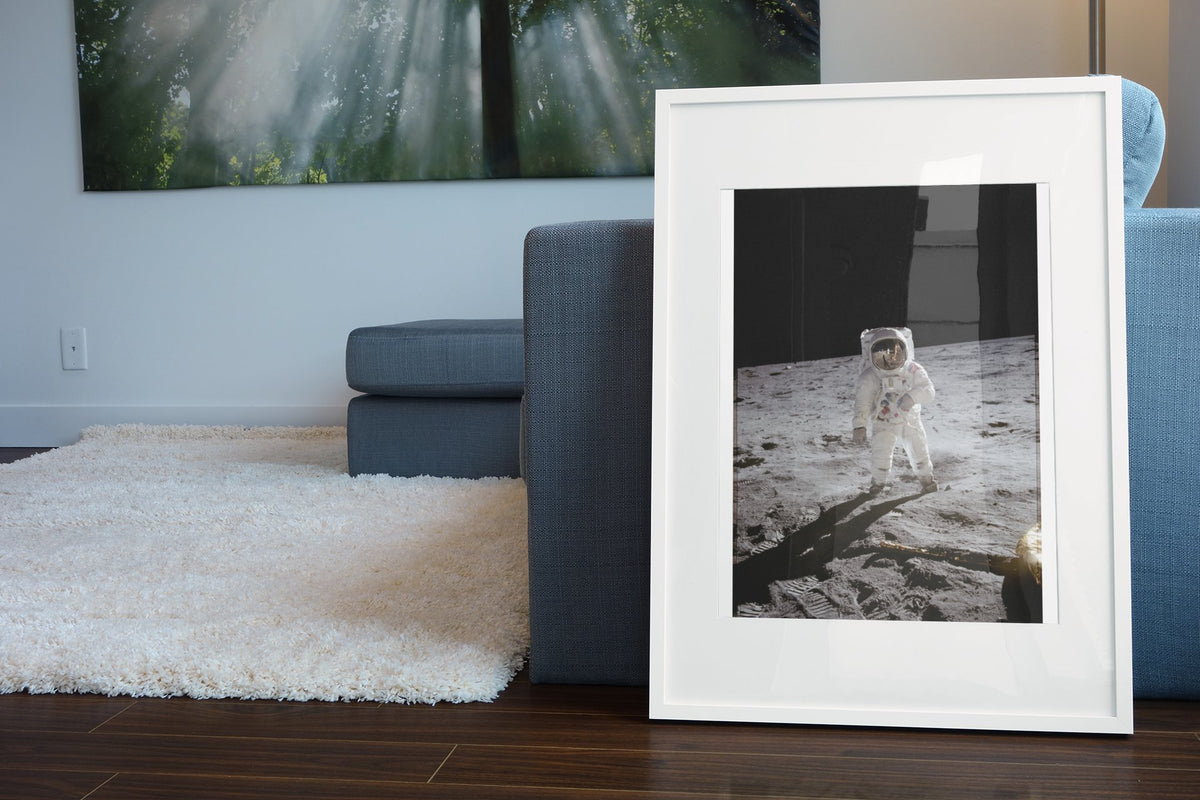 Apollo 11 Buzz Aldrin moonwalk poster in a white frame leaning beside a blue sofa