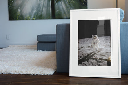 Apollo 11 Buzz Aldrin moonwalk poster in a white frame leaning beside a blue sofa