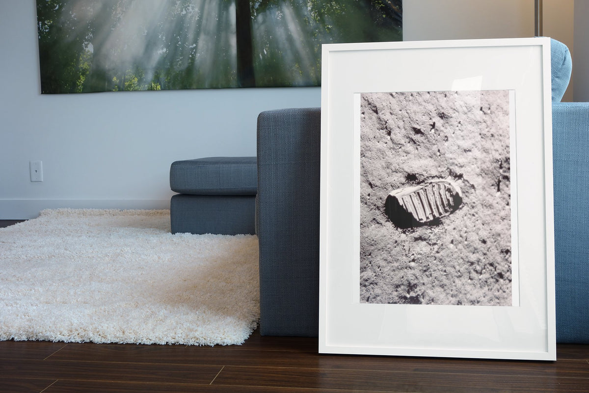 Apollo 11 bootprint on the Moon poster in a white frame leaning beside a blue sofa