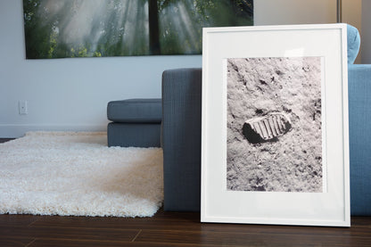 Apollo 11 bootprint on the Moon poster in a white frame leaning beside a blue sofa