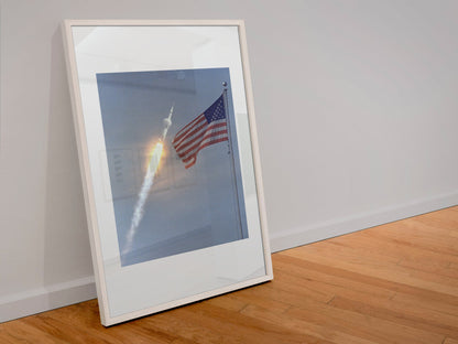 Apollo 11 rocket launch with the US flag poster in a white frame leaning against a wall