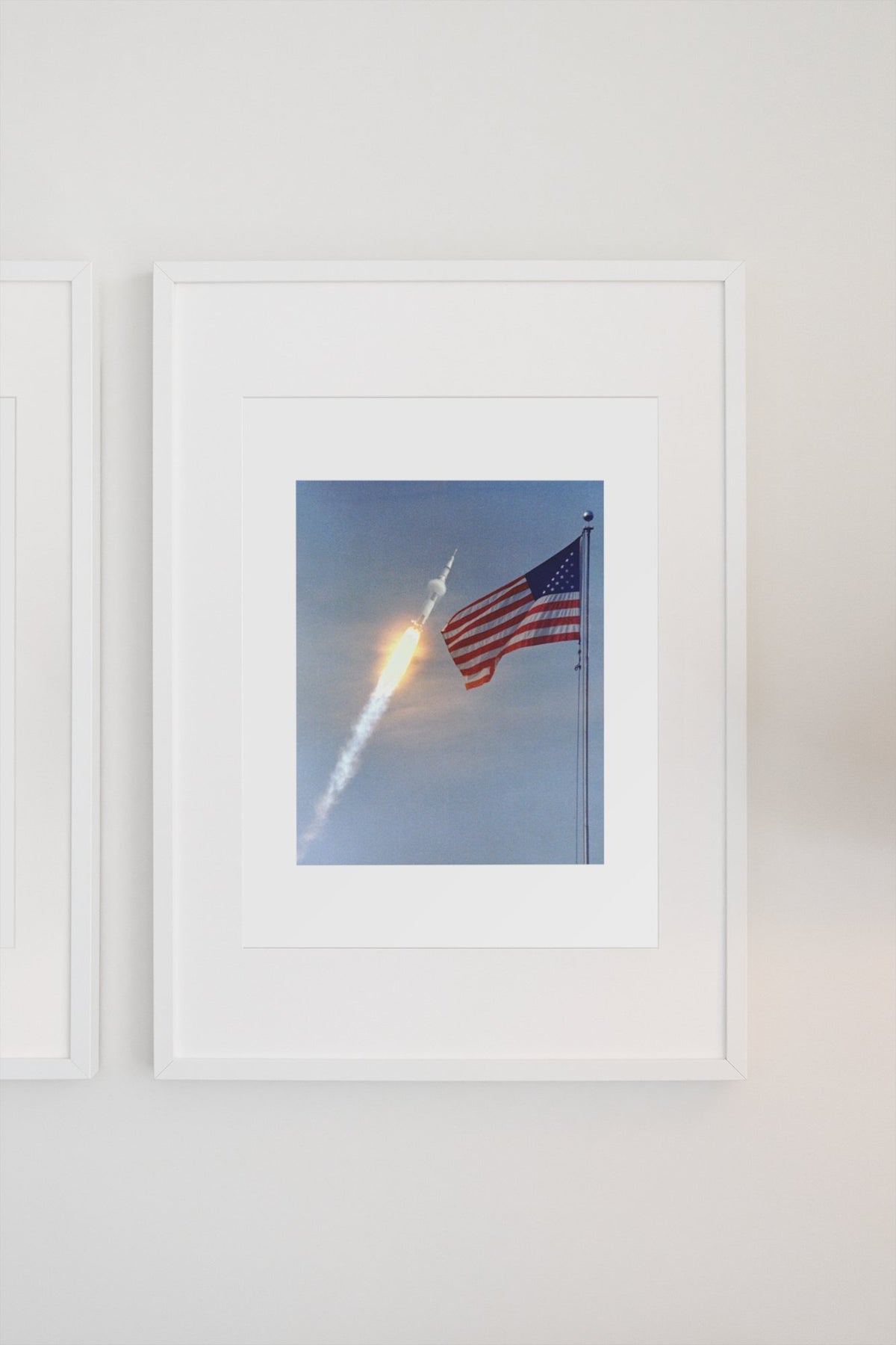Apollo 11 rocket launch with the US flag poster in a white frame on a light wall