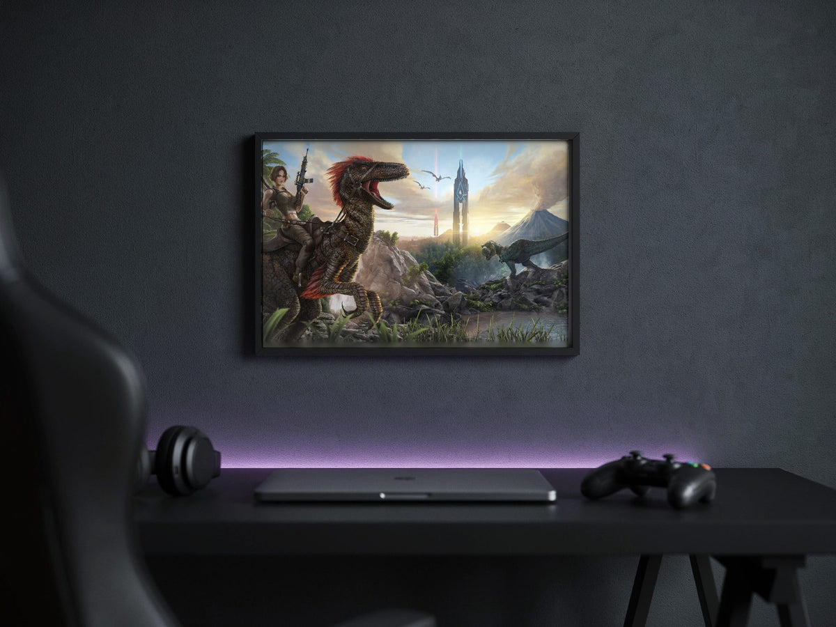 ARK: Survival Evolved Key Art poster in a black frame above a gaming desk