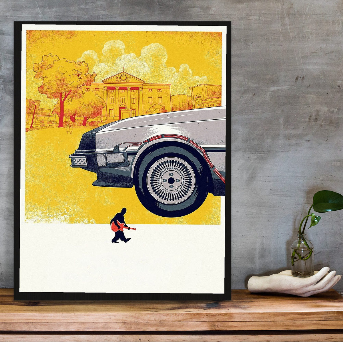 Back to the Future (1985) Movie DeLorean Illustrated Art poster in a black frame on a wooden shelf against concrete