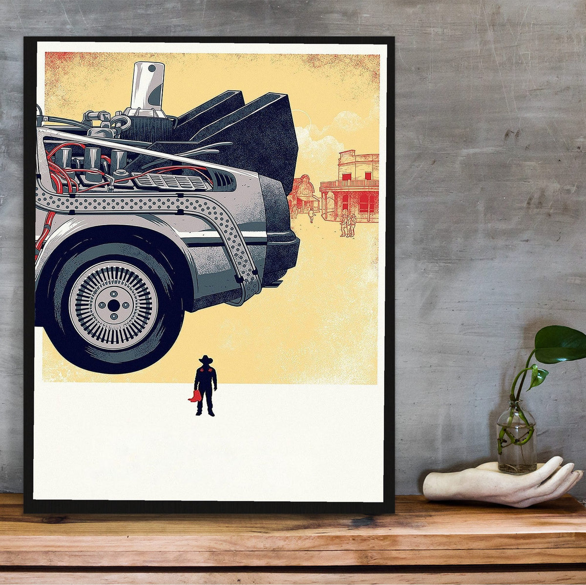 Back to the Future Part III (1990) Movie DeLorean Western Art poster in a black frame on a wooden shelf against concrete