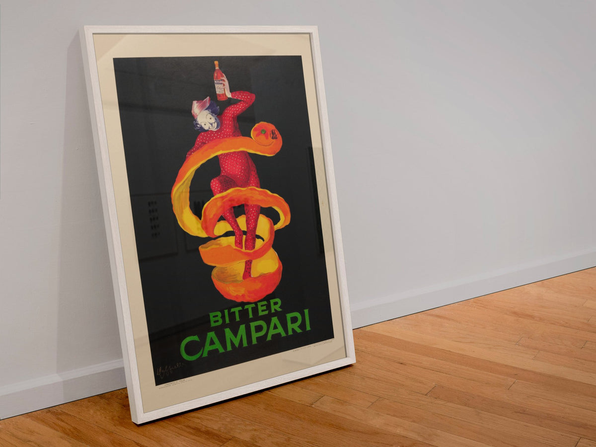 Bitter Campari by Cappiello poster in a white frame leaning against a wall