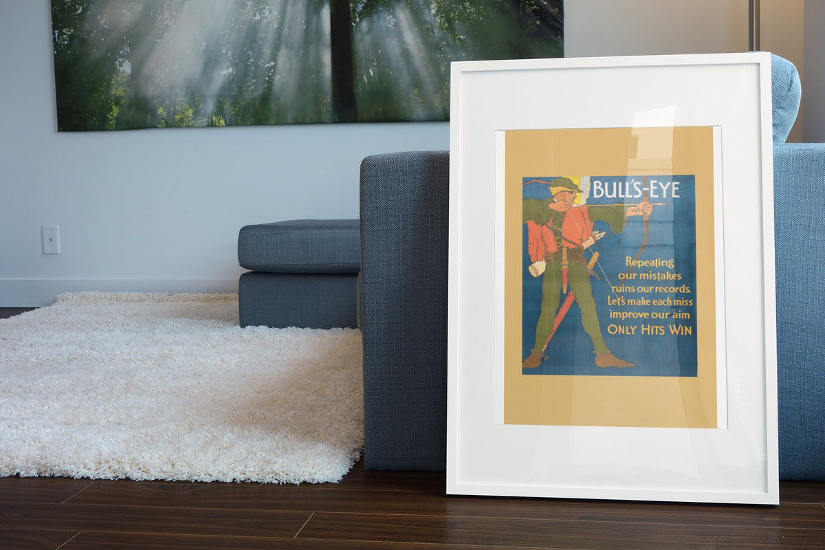 Bull’s-Eye poster in a white frame leaning beside a blue sofa
