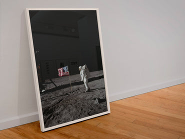 Buzz Aldrin with the US flag on the Moon poster in a white frame leaning against a wall