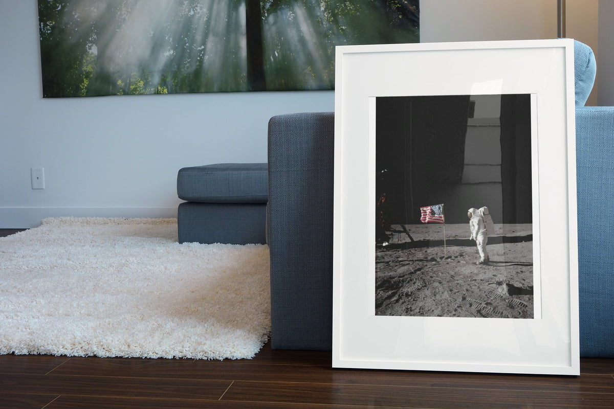 Buzz Aldrin with the US flag on the Moon poster in a white frame leaning beside a blue sofa