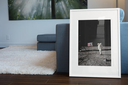 Buzz Aldrin with the US flag on the Moon poster in a white frame leaning beside a blue sofa