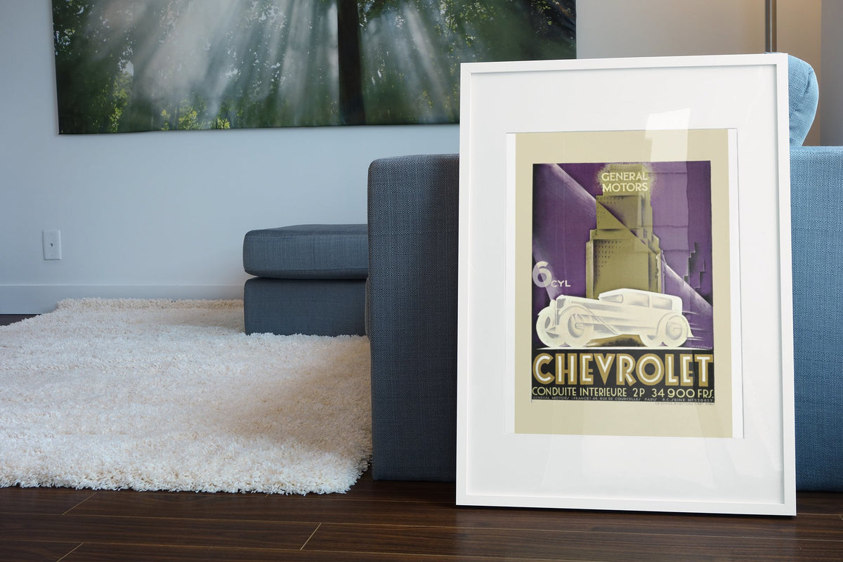 Chevrolet Conduite Intérieure poster in a white frame leaning beside a blue sofa