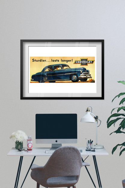 Chevrolet De Luxe 1951 poster framed on a grey wall above a desk