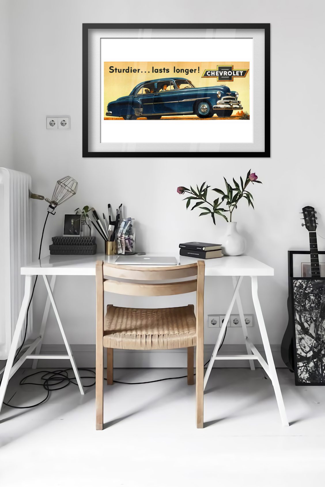 Chevrolet De Luxe 1951 poster framed above a desk in a bright white room