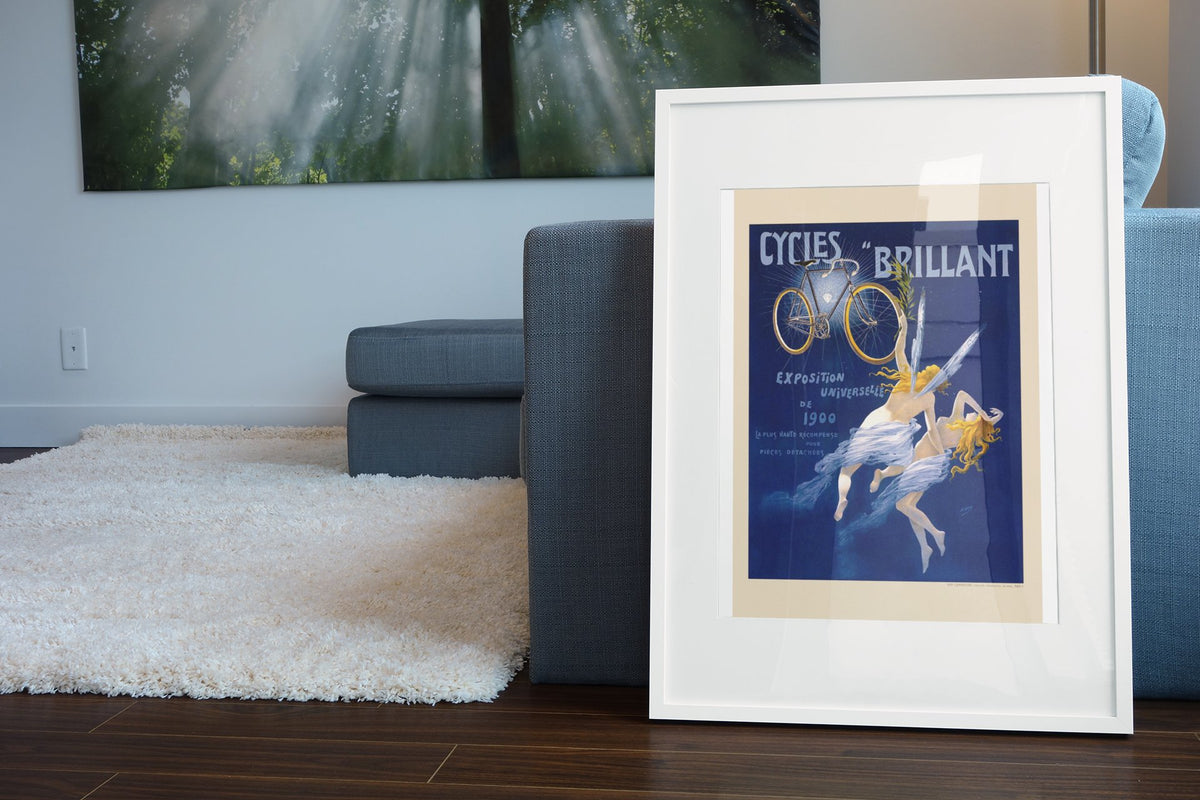 Cycles Brillant 1900 bicycle poster in a white frame leaning beside a blue sofa