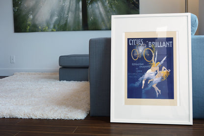 Cycles Brillant 1900 bicycle poster in a white frame leaning beside a blue sofa