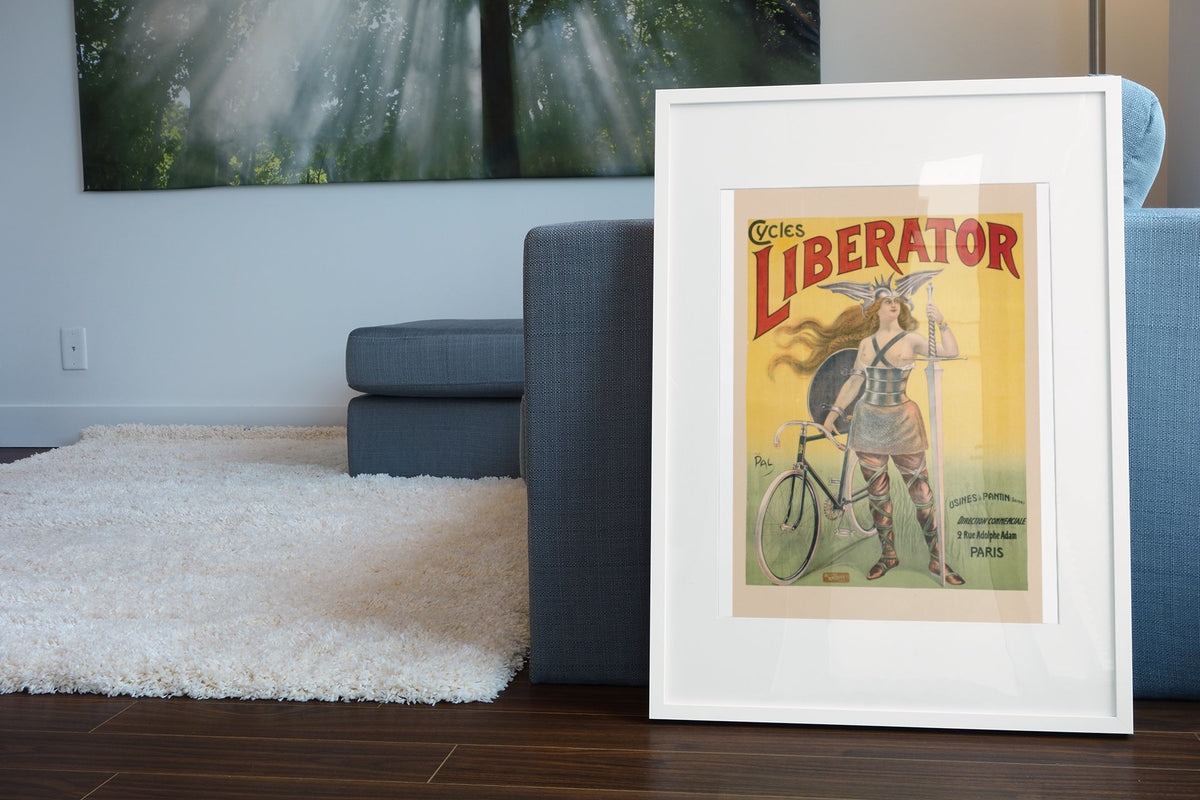 Cycles Liberator 1899 bicycle poster in a white frame leaning beside a blue sofa