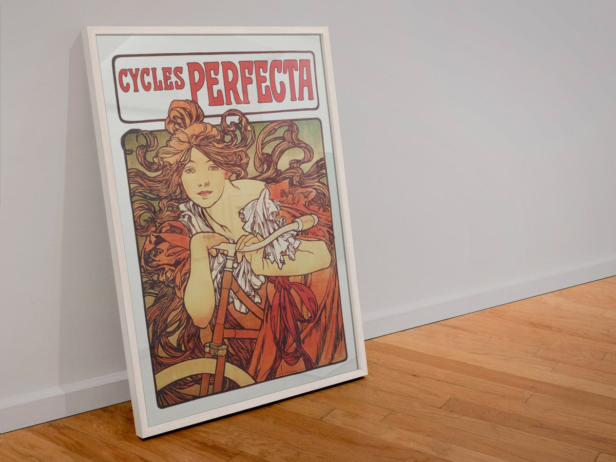 Mucha Cycles Perfecta poster in a white frame leaning against a wall