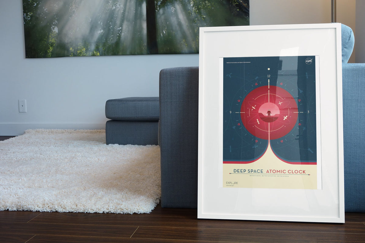 Deep Space Atomic Clock, red poster in a white frame leaning beside a blue sofa