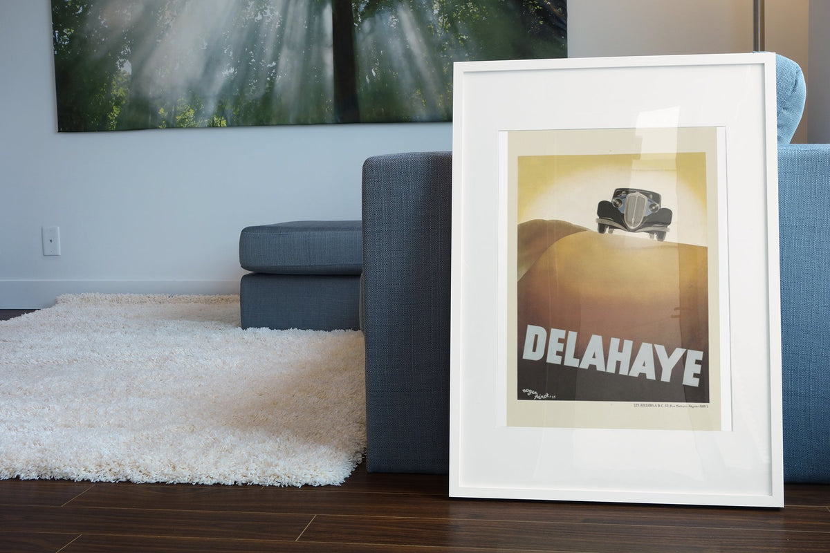Delahaye poster in a white frame leaning beside a blue sofa