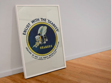 Enlist with the Seabees poster in a white frame leaning against a wall
