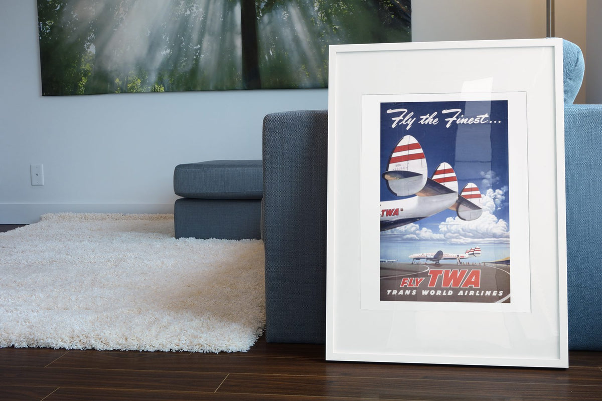 Fly the Finest Fly TWA poster leaning beside a blue sofa