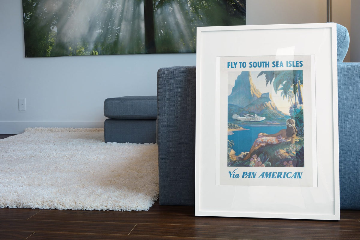 Fly to South Sea Isles Pan American poster leaning beside a blue sofa