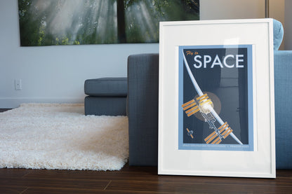 Fly to Space retro space travel poster in a white frame leaning beside a blue sofa