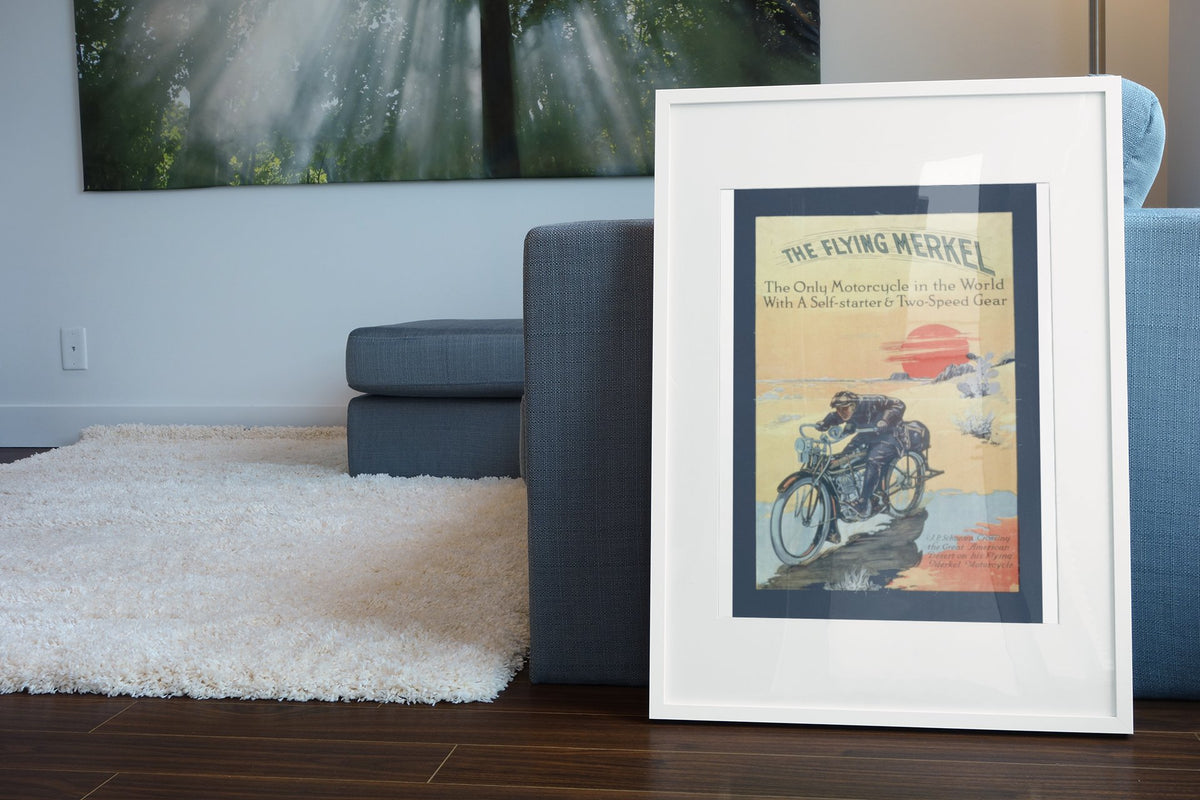 The Flying Merkel 1913 poster in a white frame leaning beside a blue sofa