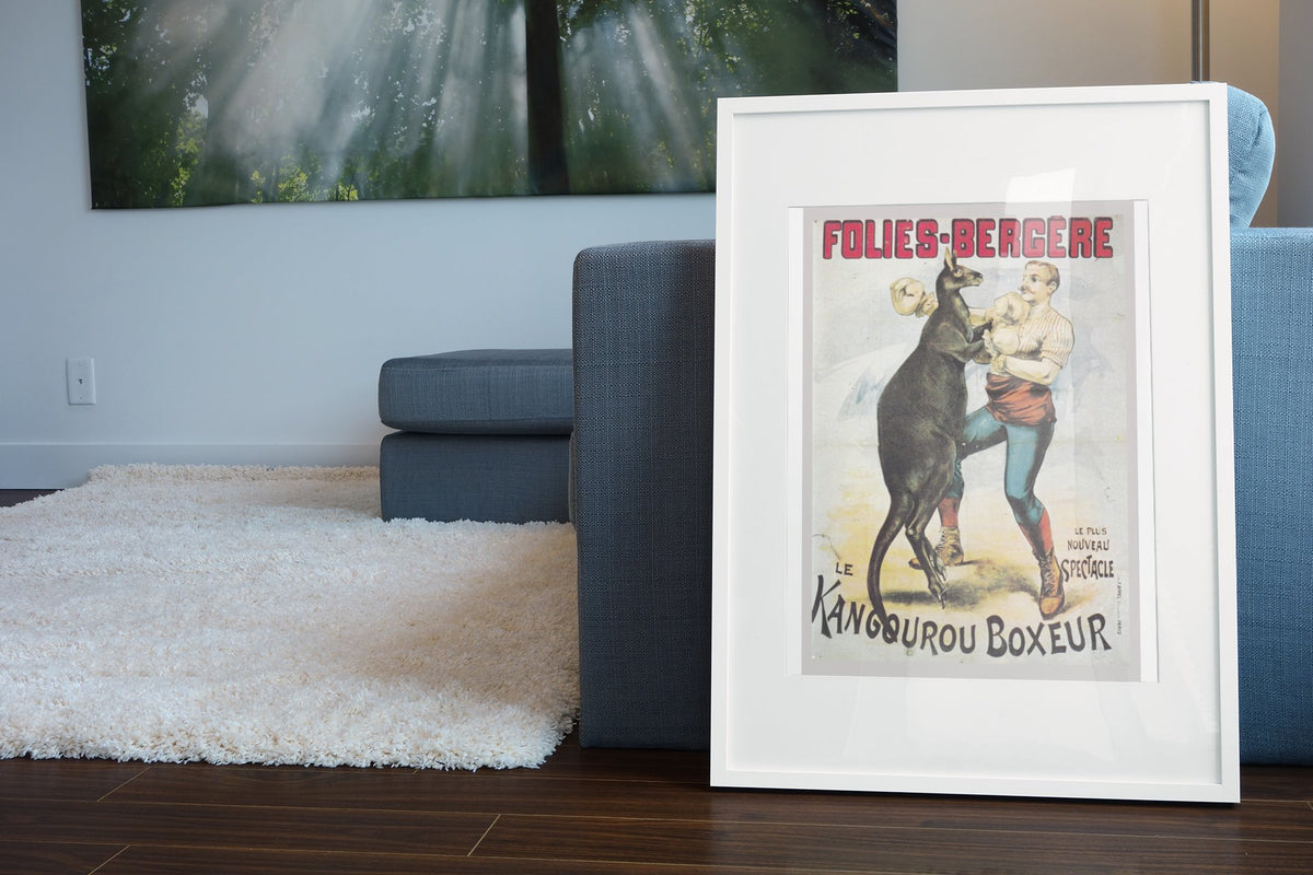 Folies-Bergère Kangaroo Boxer poster in a white frame leaning beside a blue sofa